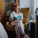 A woman sits in a cozy armchair indoors, enjoying a peaceful reading moment.