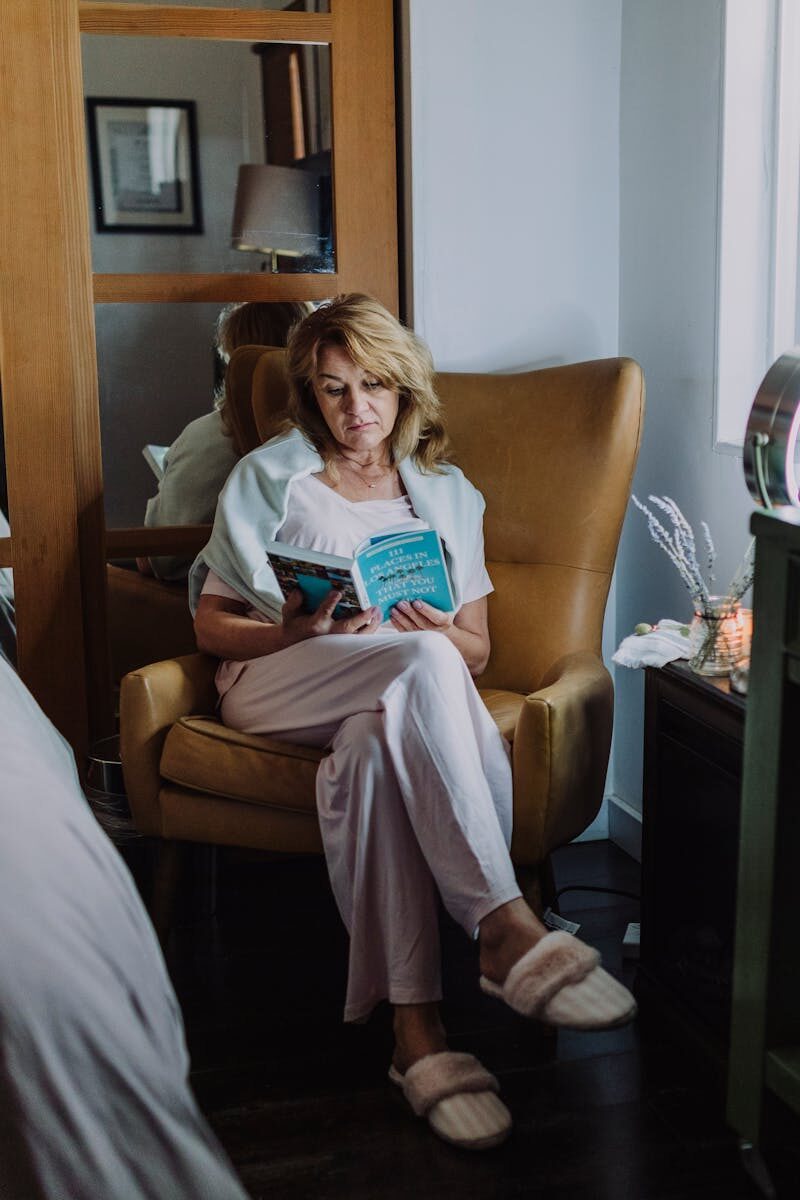 A woman sits in a cozy armchair indoors, enjoying a peaceful reading moment.