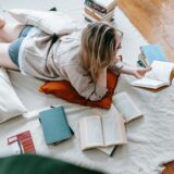 Woman lounging on floor, surrounded by open books, embodying leisure and literacy at home.