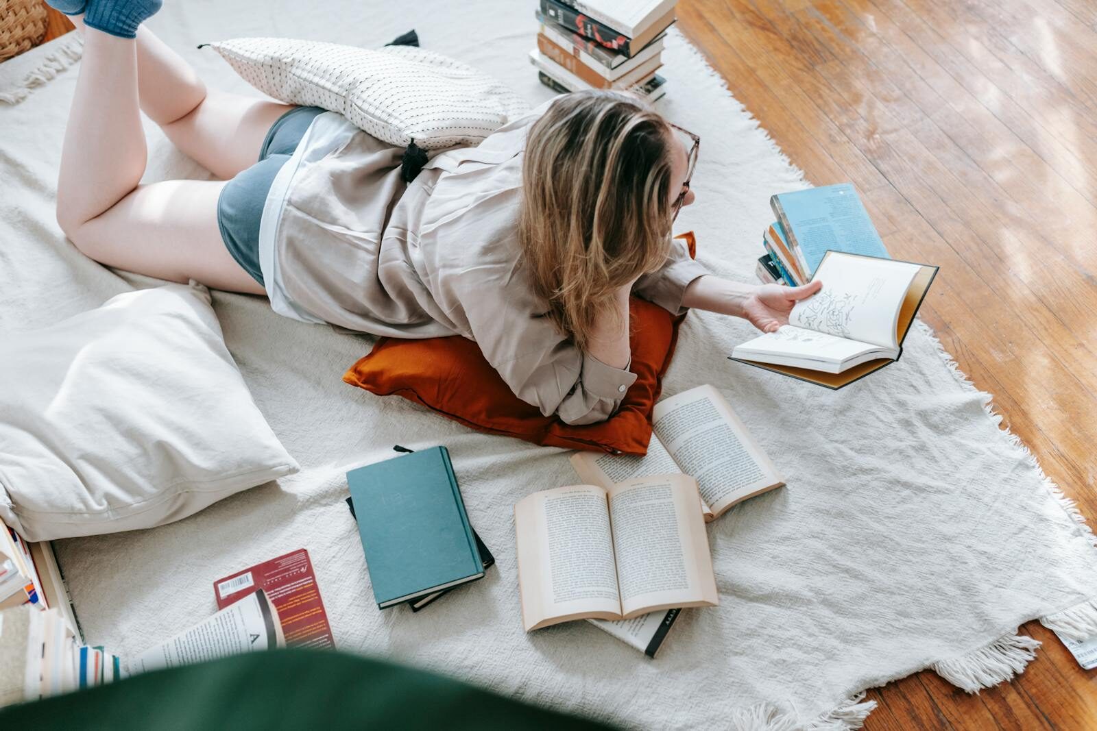 Woman lounging on floor, surrounded by open books, embodying leisure and literacy at home.