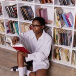 A woman enjoying a book sits in front of modern bookshelves indoors.
