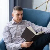 Adult man reading in an armchair indoors, showcasing relaxation and leisure.