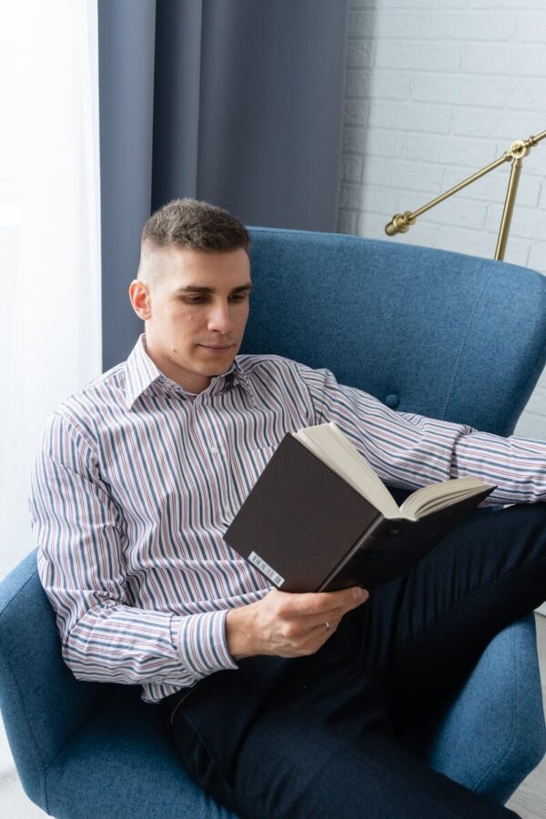 Adult man reading in an armchair indoors, showcasing relaxation and leisure.