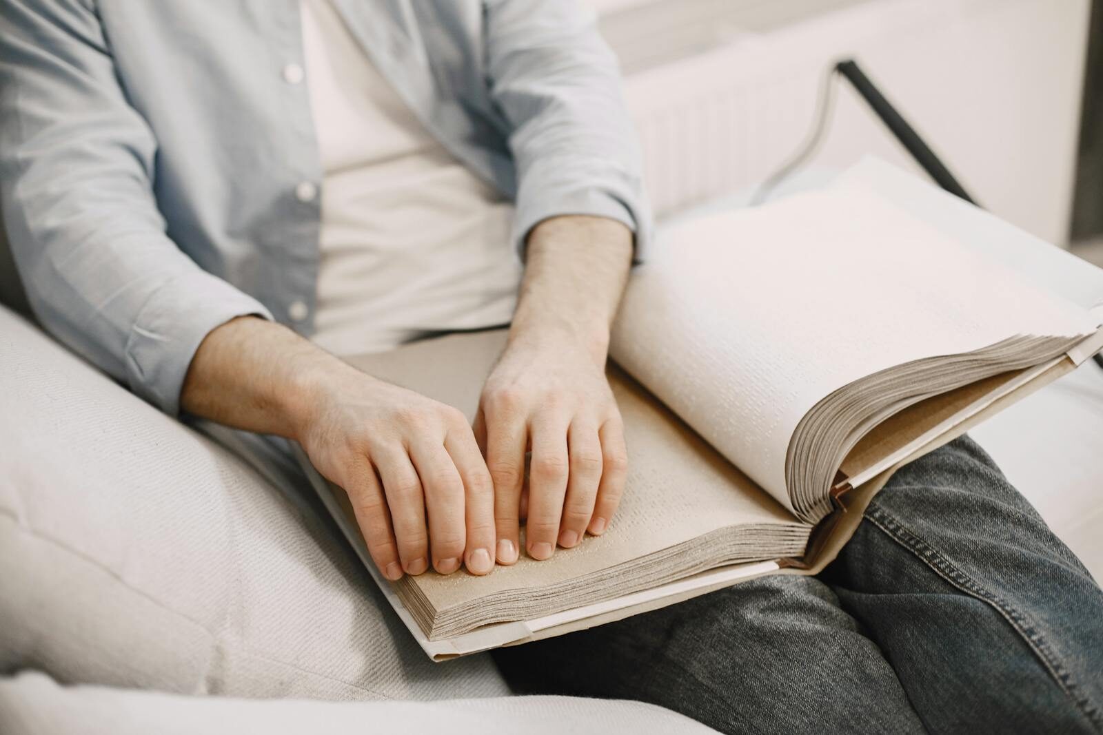 An adult reading a braille book indoors, highlighting visual impairment awareness.