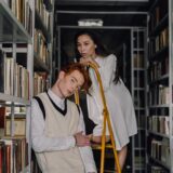Fashionable young adults posing on a ladder among library bookshelves.