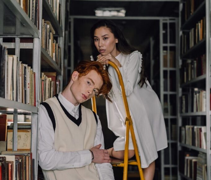 Fashionable young adults posing on a ladder among library bookshelves.