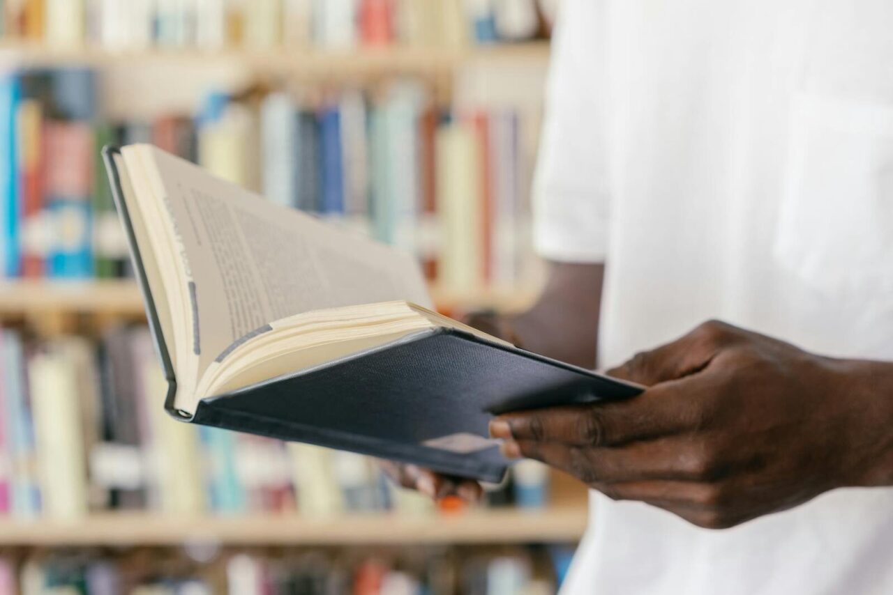 A person reads a book in a library, focusing on hands holding an open book.