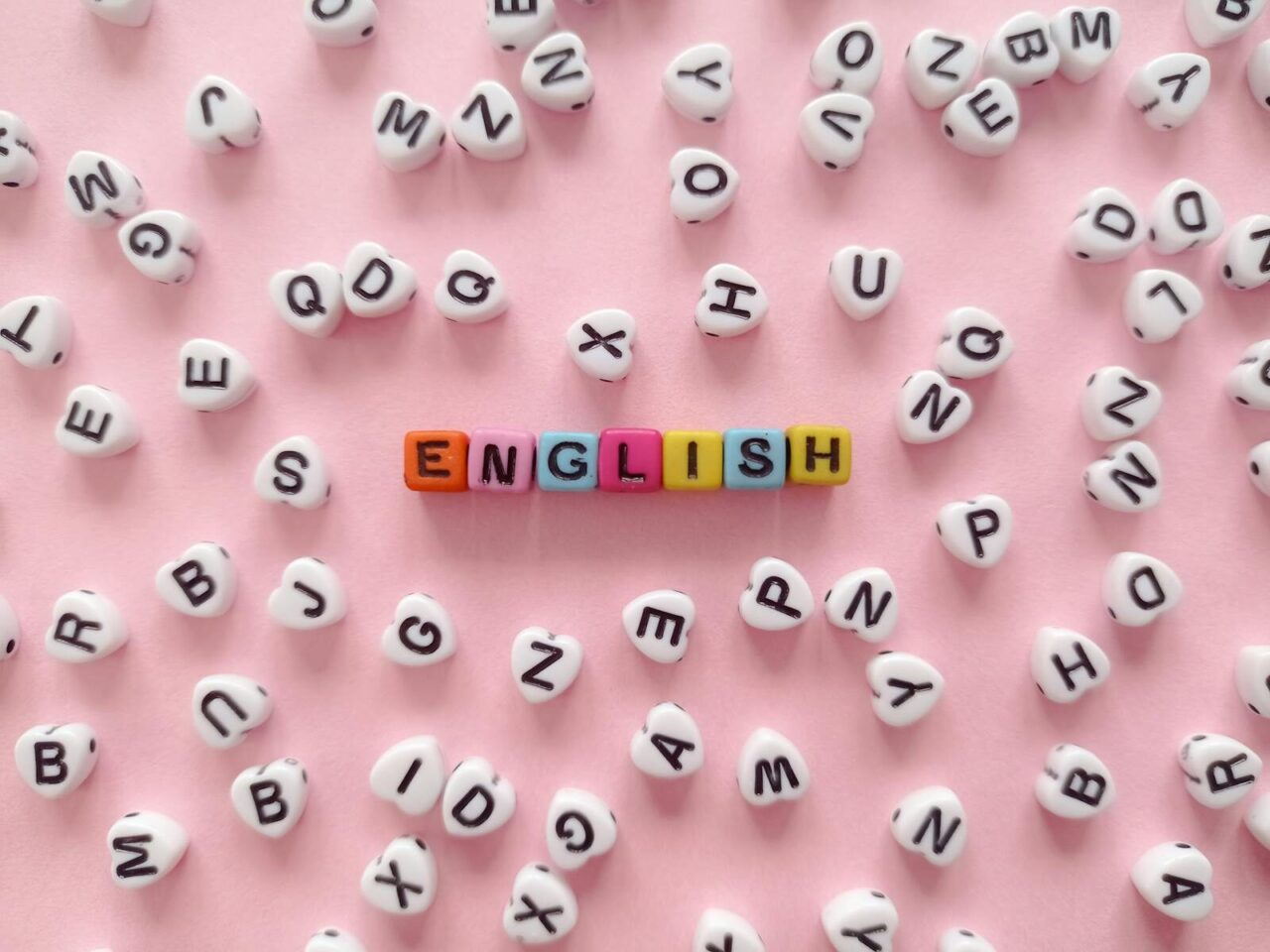 Scattered letter beads form the word 'English' on a pink background, symbolizing language learning.