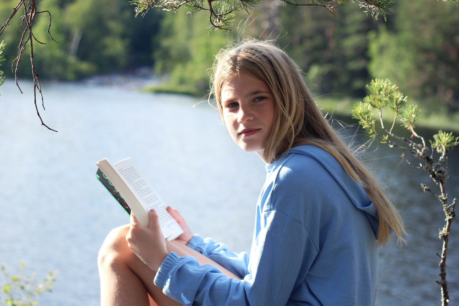 Young woman reads a book by the lake.